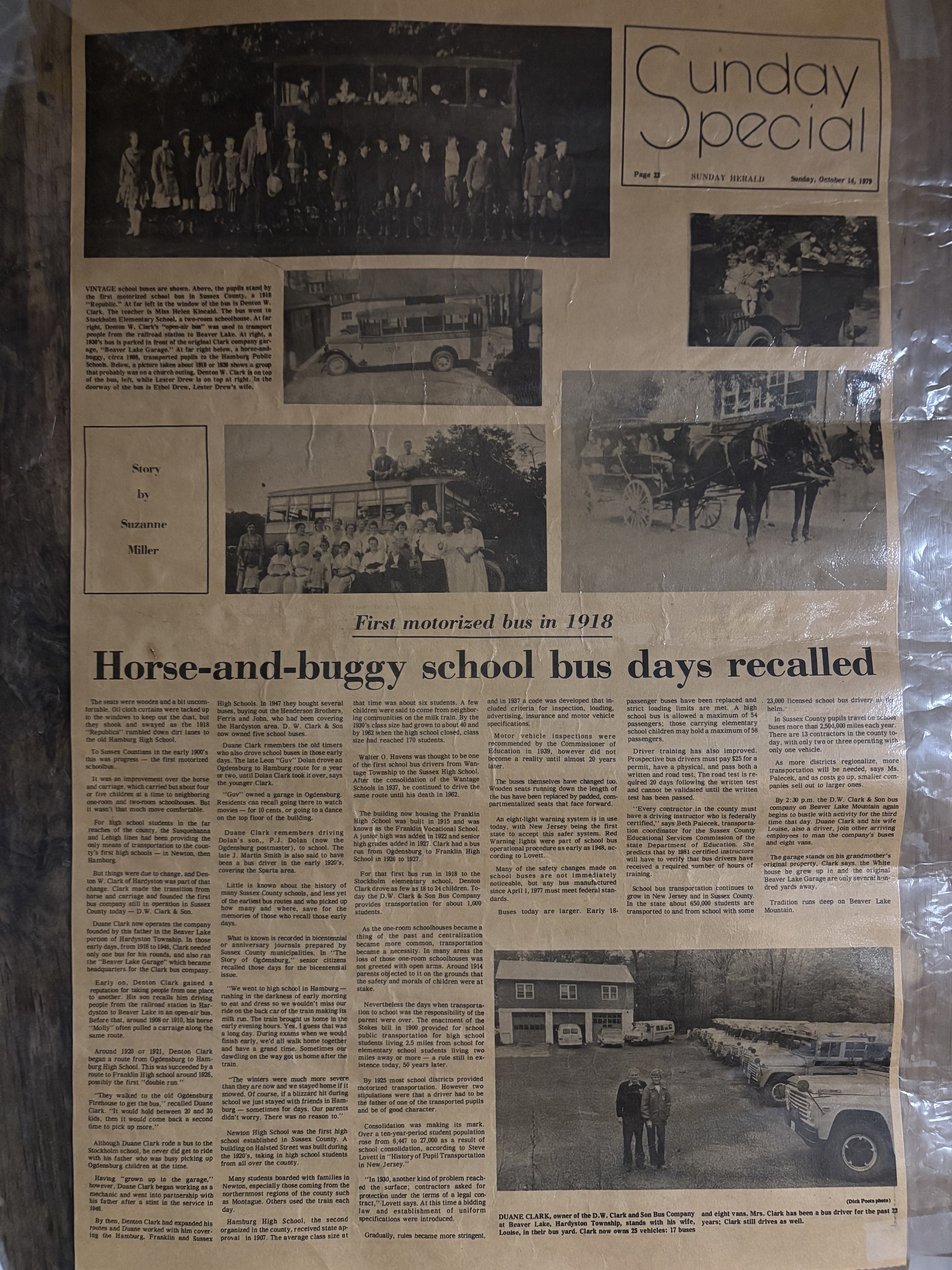 Smiling school bus driver seated behind the wheel of a yellow school bus, wearing a D W Clark & Son uniform